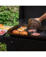 A person uses a grill press to flatten a hamburger patty while cooking it on a griddle.