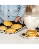 A person uses a griddle to make pancakes, topping them with blueberries as they cook.
