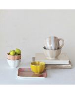 A stack of colorful bowls, cups, and plates adorned with fresh apples on top, showcasing a vibrant kitchen setting