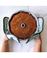 A person holding a freshly baked cake in a round pan, smiling and presenting it to the camera.