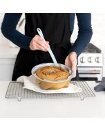 A woman in an apron holds a spatula above a cake, preparing to serve or decorate it with care.