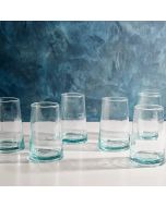 Six clear glass tumblers arranged neatly on a wooden table, reflecting light and showcasing their transparent design.
