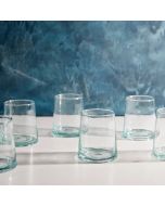  Six empty glass tumblers arranged neatly on a wooden table, reflecting light in a bright setting.