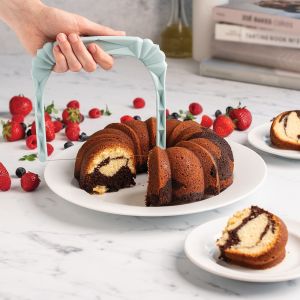 A hand grips a blue-handled Nordic Ware Bundt Slicer, poised to slice a bundt cake.