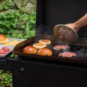 A person uses a grill press to flatten a hamburger patty while cooking it on a griddle.