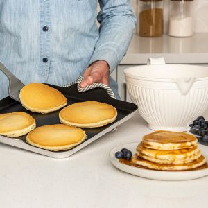 A person uses a griddle to make pancakes, topping them with blueberries as they cook.