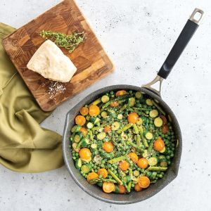 A pan filled with vegetables and a slice of cheese on a wooden table.