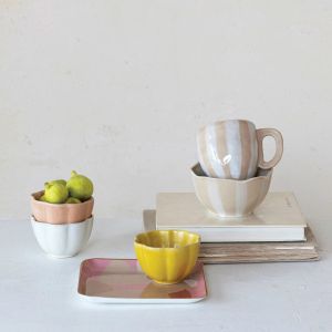  A stack of colorful bowls, cups, and plates adorned with fresh apples on top, showcasing a vibrant kitchen setting