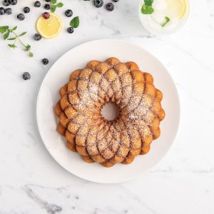 A bundt cake on a white plate, garnished with fresh blueberries and lemon slices for a vibrant presentation.