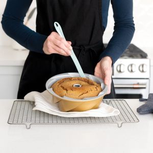 A woman in an apron holds a spatula above a cake, preparing to serve or decorate it with care.