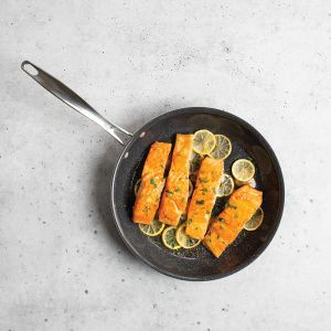 Salmon fillets cooking in a skillet, garnished with fresh lemon slices for added flavor.