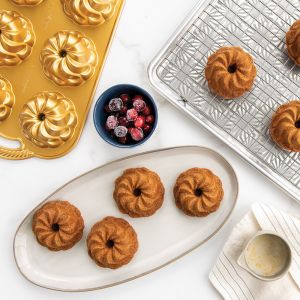 A table displays bundt pans alongside an assortment of mini muffins, showcasing a variety of baked goods.
