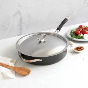 A covered pan with a wooden spoon rests on a white countertop, ready for cooking or serving a meal.
