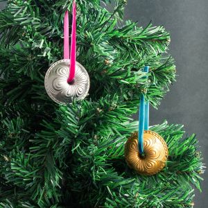 Two shiny metal ornaments hang from a decorated Christmas tree, reflecting light and adding festive charm.