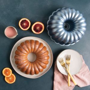 A bundt cake on a plate beside a plate of vibrant blood oranges, showcasing a colorful dessert arrangement.