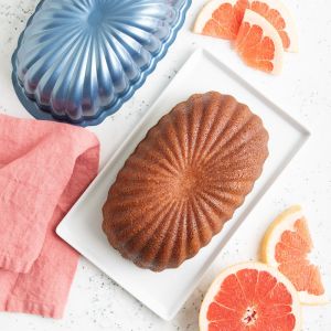 A bundt cake on a plate beside fresh grapefruits, showcasing a vibrant dessert and fruit arrangement.