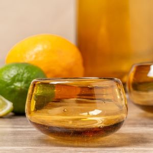 A glass bowl containing a bright orange and a fresh lime, showcasing their vibrant colors and textures.
