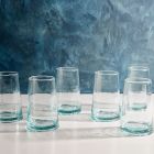 Six clear glass tumblers arranged neatly on a wooden table, reflecting light and showcasing their transparent design.
 Image