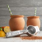 Two cups with lime slices on the rim and a spoon resting beside them, set against a neutral background. Image