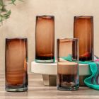Four tall glass vases filled with brown liquid, arranged in a row on a neutral background. Image