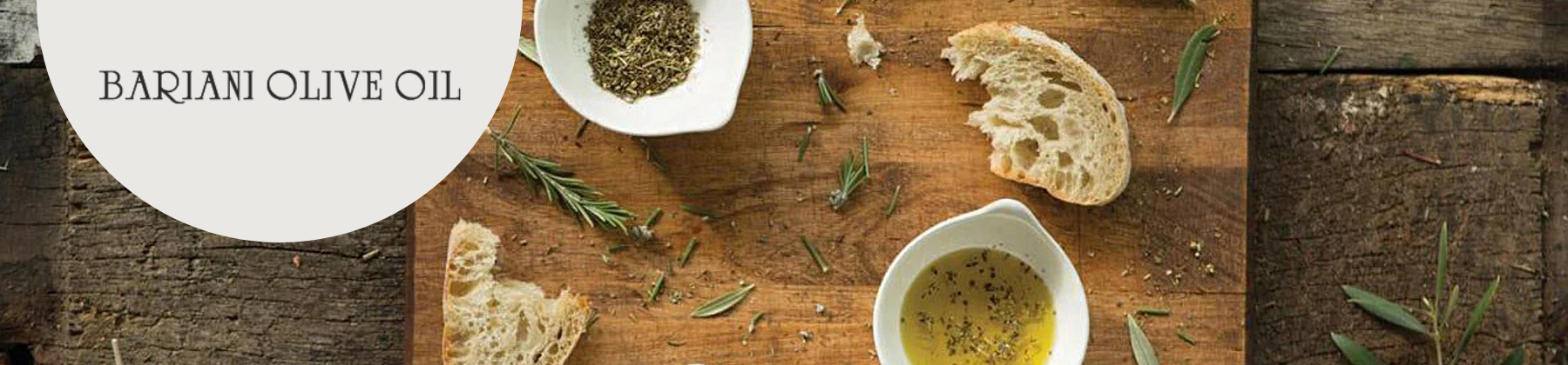 Photo of Bariani olive oil on a table with herbs, ready to be served with bread.