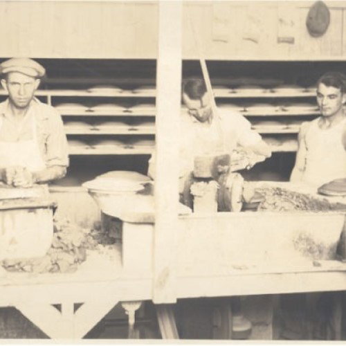 a vintage black and white image shows men on the pottery production line